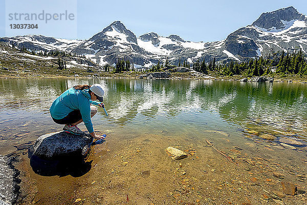 Eine Frau füllt während einer Wanderung an einem heißen Sommertag in den Bergen um Pemberton  British Columbia  Kanada  eine Wasserflasche mit einem Filter aus einem Bergsee auf.