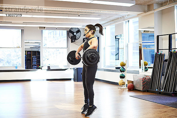 Seitenansicht einer einzelnen weiblichen Fitnesstrainerin  die im Fitnessstudio Gewichte hebt.