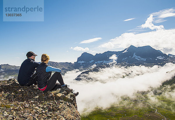 Ganzaufnahme eines Paares  das sitzt und den Blick auf die über dem Nebel aufsteigenden Berge genießt  Borgafjordur Eystri  Island