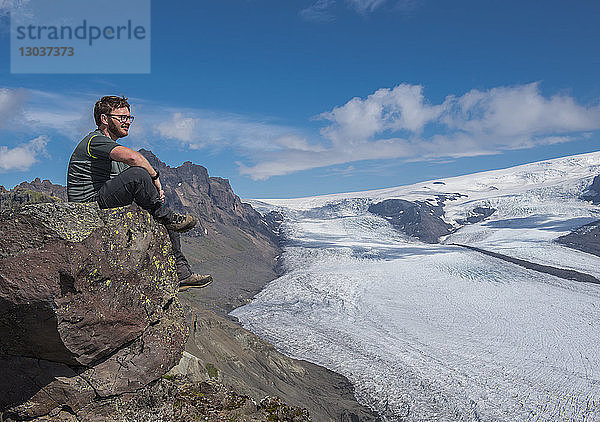 Seitenansicht eines männlichen Wanderers  der auf einem Felsen in der Nähe des Skaftafellsjokull-Gletschers sitzt  Vatnajokull-Nationalpark  Island