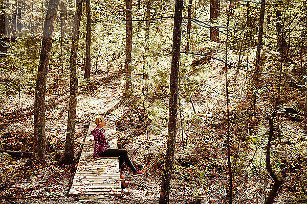 Seitenansicht einer blonden Frau in Sportkleidung  die im Wald sitzt