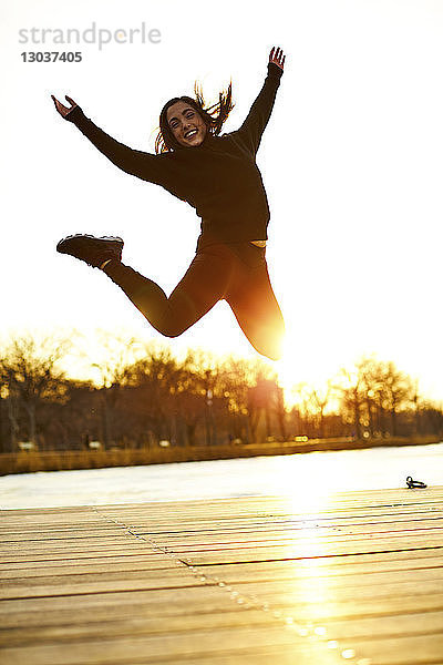 Junge Frau springt bei Sonnenuntergang in Freude