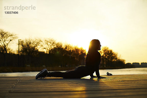 Silhouette einer Frau in einer nach oben gerichteten Hundestellung beim Yoga bei Sonnenuntergang