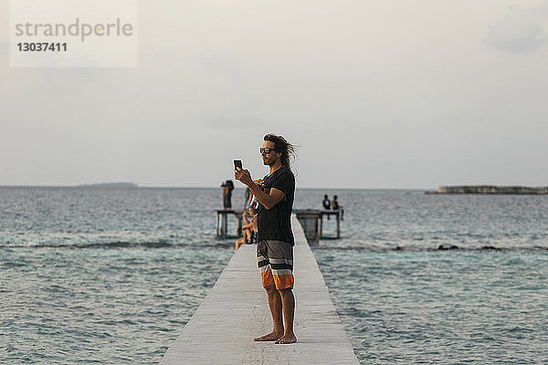 Seitenansicht eines einzelnen mÃ?nnlichen Touristen  der ein Foto auf einem Pier macht â€ Thulusdhoo  Male  Malediven