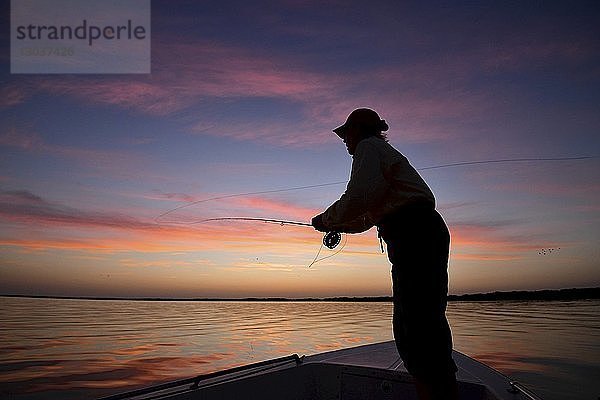 Silhouette eines einzelnen Mannes beim Fliegenfischen von einem Motorboot aus bei Sonnenuntergang in Campeche  Mexiko