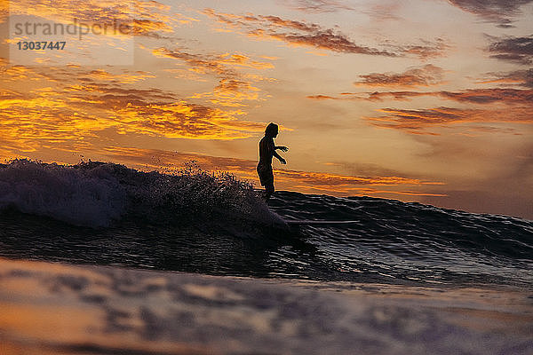 Silhouette eines mÃ?nnlichen Surfers  der bei Sonnenuntergang auf einer Welle im Meer reitet  Changgu  Bali  Indonesien