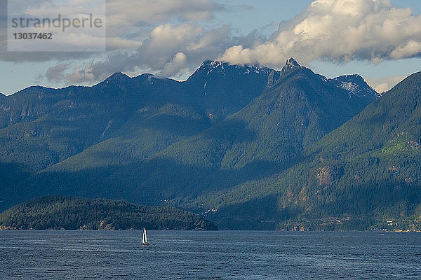 Fernblick auf ein Segelboot  das im Meer segelt  in der Nähe von Bergen am Ufer  Vancouver  British Columbia  Kanada