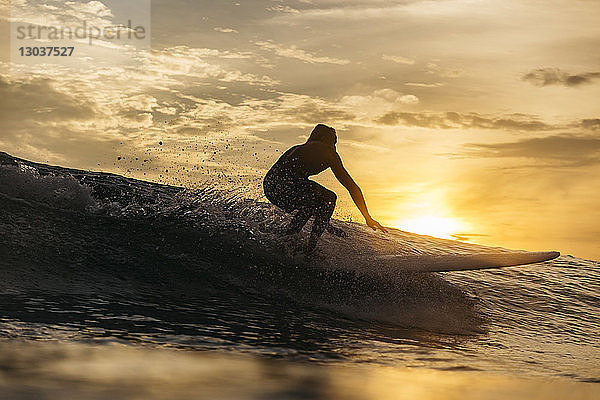 Silhouette eines mÃ?nnlichen Surfers  der bei Sonnenuntergang auf einer Welle im Meer reitet  Changgu  Bali  Indonesien