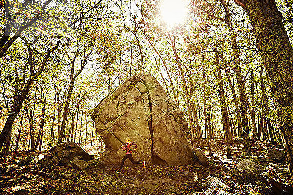 Seitenansicht einer einzelnen Frau  die an einem Felsen im Wald vorbei joggt