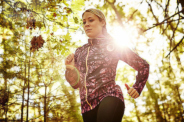 Taillenaufnahme einer einzelnen blonden Frau in Sportkleidung beim Joggen in einem Wald