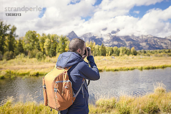 Mann mit Rucksack fotografiert stehend am Flussufer