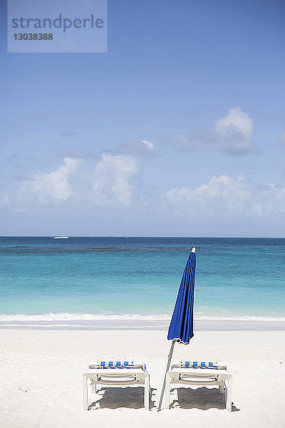 Liegestühle und Sonnenschirm am Strand gegen den Himmel am sonnigen Tag