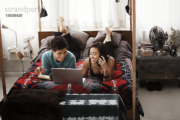 Glückliches Paar benutzt Laptop  während es zu Hause auf einem Himmelbett liegt