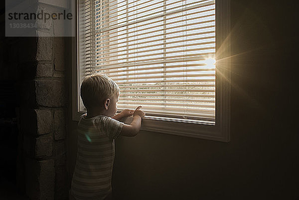 Zu Hause stehender Junge spielt mit Fensterläden