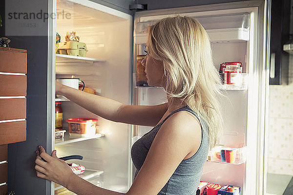 Seitenansicht eines Teenager-Mädchens  das im Kühlschrank in die Küche schaut