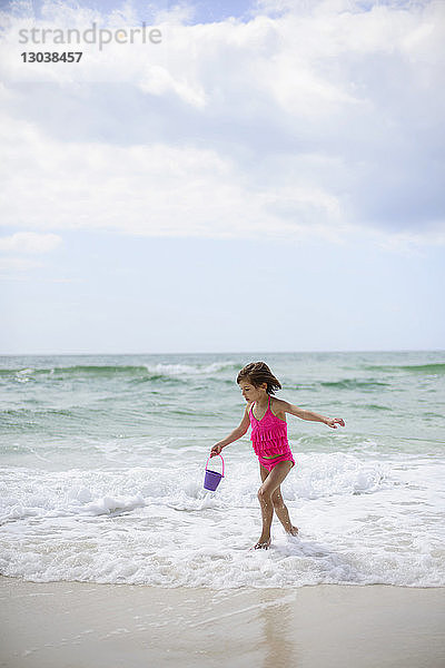 Mädchen spielt am Strand mit Eimer gegen bewölkten Himmel