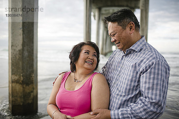 Glückliches Paar steht unter Pier am Strand