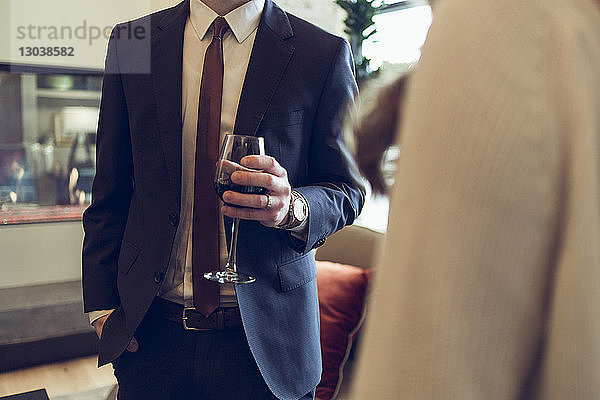 Mittelteil eines Geschäftsmannes  der Weinglas hält  während er mit einem Kollegen im Hotel steht