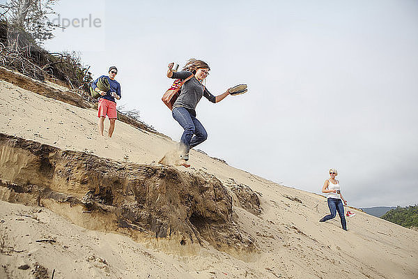 Frau springt von Sanddüne und genießt mit Freunden am Strand