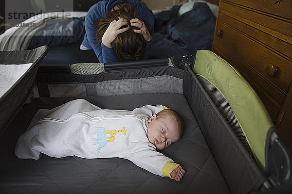 Süßes Mädchen schläft im Gitterbett von depressiver Mutter zu Hause im Bett