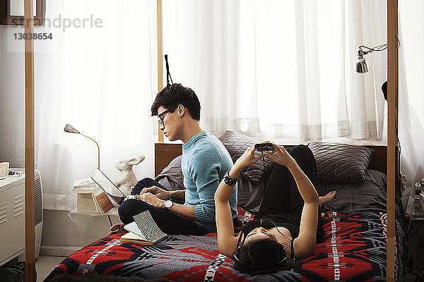 Ehepaar nutzt Laptop und Smartphone  während es sich im Schlafzimmer entspannt