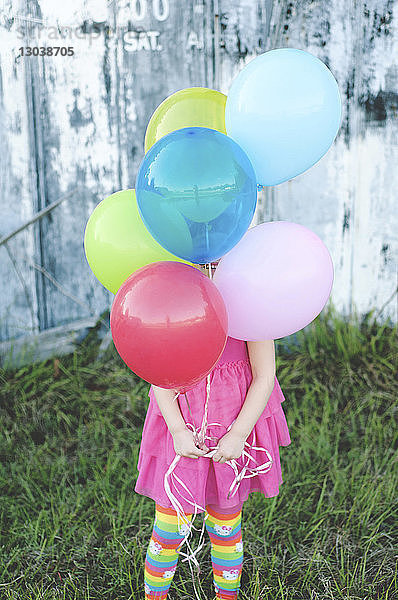 Mädchen in der Mitte hält bunte Luftballons in der Hand  während sie auf einem Grasfeld im Park steht