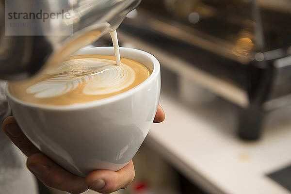 Beschnittene Abbildung von Händen  die ein Muster mit Sahne auf Kaffee machen