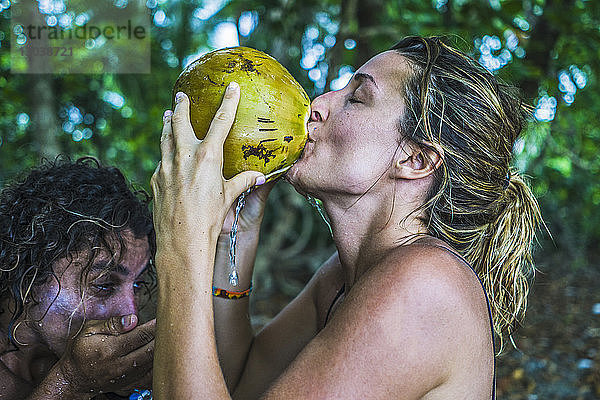 Seitenansicht eines Paares  das im Wald aus frischer Kokosnuss trinkt