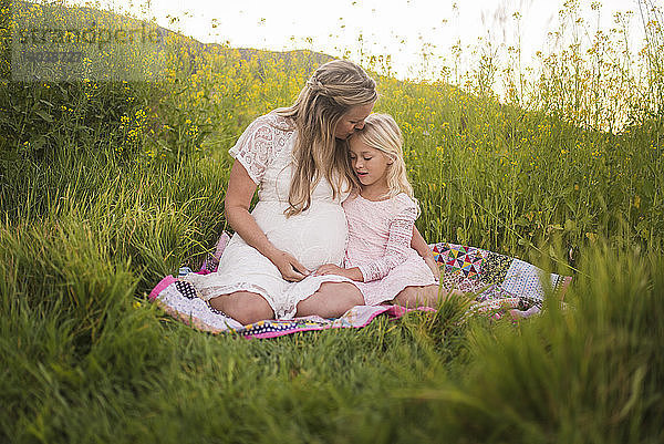 Glückliche Mutter küsst Tochter auf die Stirn  während sie im Park sitzt