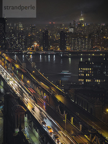 Lichtspuren auf der Brücke über den Fluss in der beleuchteten Stadt bei Nacht