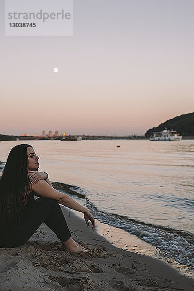 Seitenansicht einer nachdenklichen Frau  die bei Sonnenuntergang am Strand vor klarem Himmel wegschaut