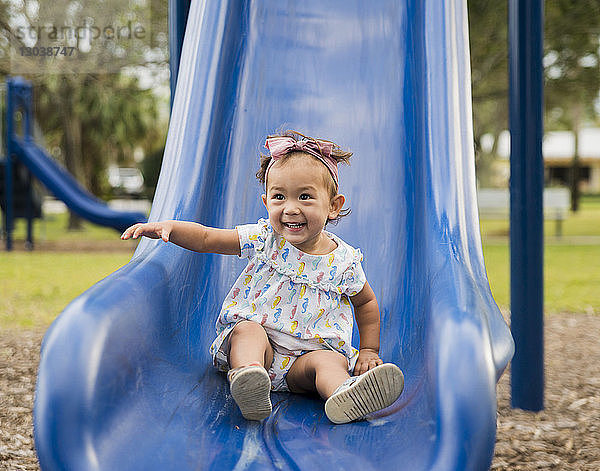 Süßes fröhliches Mädchen rutscht auf einer Rutsche auf dem Spielplatz