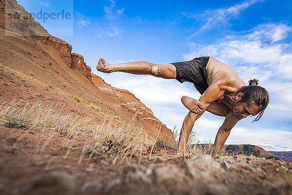 Entschlossener Mann ohne Hemd  der im Bridger-Teton National Forest Yoga-Haltung gegen den Himmel praktiziert
