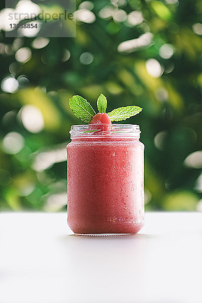 Nahaufnahme von Erdbeer- und Minzeblättern auf Konfitüre im Glas bei Tisch