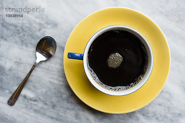 Draufsicht auf schwarzen Kaffee in Tasse und Löffel auf Marmortisch