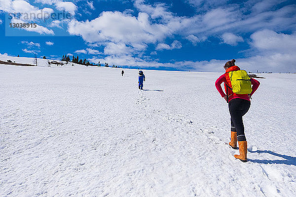 Rückansicht von Wanderern  die auf schneebedecktem Feld vor bewölktem Himmel gehen