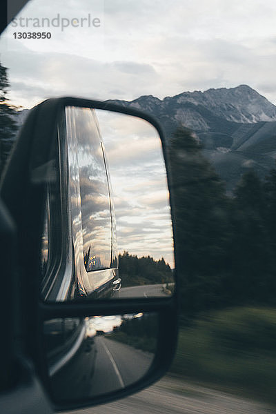 Bewölkter Himmel spiegelt sich am Seitenspiegel des Autos