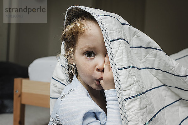 Porträt eines Mädchens beim Daumenlutschen mit Decke auf dem Bett zu Hause