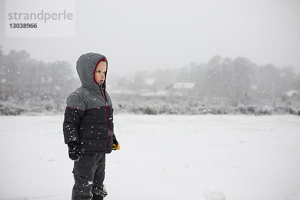 Junge trägt warme Kleidung  während er bei Schneefall auf verschneitem Feld steht