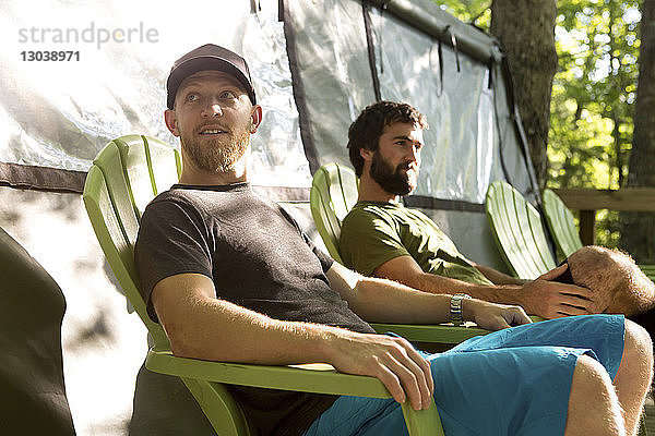 Freunde sitzen auf Stühlen und entspannen im Zelt auf einem Campingplatz im Wald