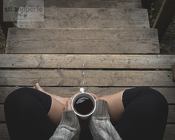 Draufsicht einer Frau  die eine Kaffeetasse hält  während sie auf einer Treppe sitzt