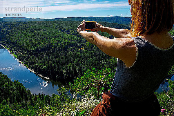 Frau fotografiert Landschaft mit Smartphone bei Sonnenschein