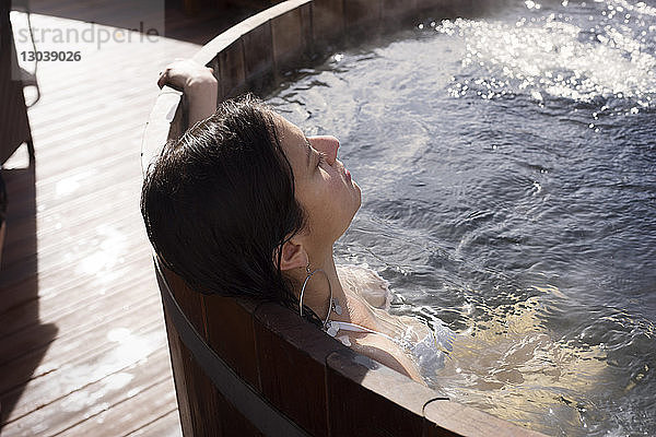 Frau entspannt sich an einem sonnigen Tag in einer Holzbadewanne