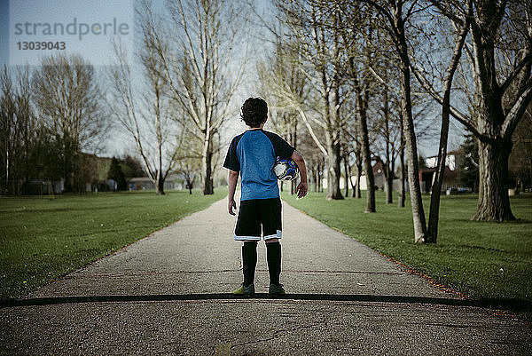 Rückansicht eines Teenagers  der einen Fussball hält  während er auf einem Fussweg steht