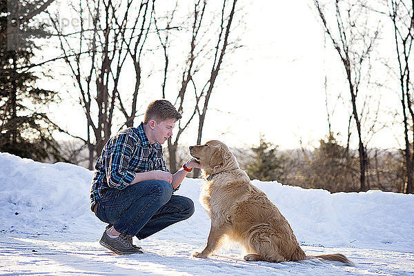 Teenager Junge streichelt Hund  während er auf schneebedecktem Feld kauert