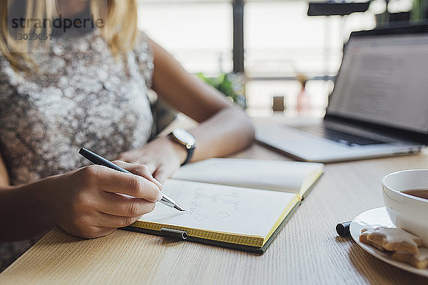 Ausgeschnittenes Bild einer Geschäftsfrau  die im Heimbüro am Tisch sitzt und in ihr Tagebuch schreibt