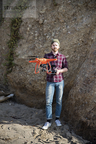 Mann fliegt Drohne in voller Länge  während er gegen eine Felsformation steht