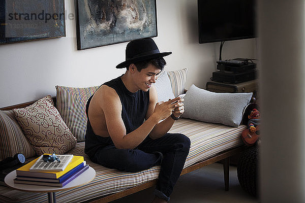 Glücklicher Mann mit Smartphone zu Hause auf dem Sofa sitzend