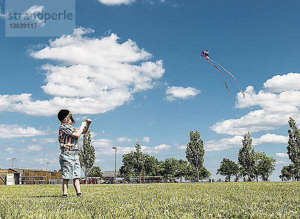 Junge in voller Länge mit Drachen mit amerikanischer Flagge im Park vor bewölktem Himmel