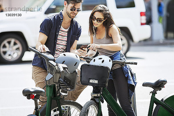 Paar  das ein Smartphone benutzt  während es mit Fahrrädern auf der Straße steht